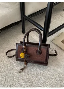 Detailansicht der braunen Handtasche mit Plüschanhänger und Logo auf beigem Teppich
