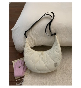 Dettaglio borsa beige trapuntata con tracolla nera regolabile su tappeto accogliente