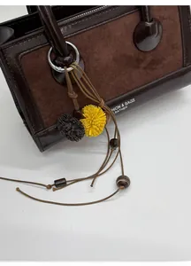 Detail einer dunkelbraunen Ledertasche mit Wildledereinsätzen und Bommel-Anhänger