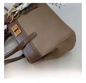 Detail of brown canvas and leather handbag with gold twist lock and woven handle