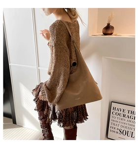 Brown leather hobo tote bag featuring a wide shoulder strap in a minimalist interior setting