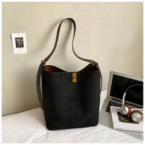 Detail of black suede tote bag with golden square buckle next to laptop and headphones