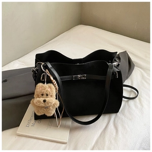 Black vintage leather tote bag with a cute brown puppy plush charm on a white bed