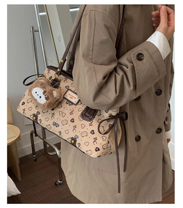 Detail of beige tote bag with monogram print and brown leather trim on model