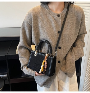 Détail d'un sac bandoulière en daim noir avec gaufrage et breloque en perles colorées