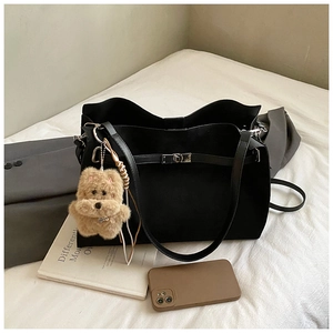 Detail view of large black matte tote bag with metal twist lock and plush bear charm