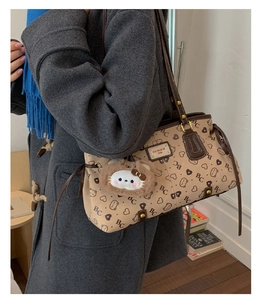 Close-up of beige vintage shoulder bag with bear print, plush charm, and logo plaque