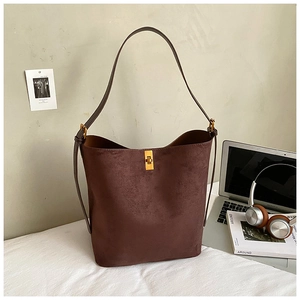 Detail of dark brown suede bucket bag with gold buckle next to a laptop and magazine