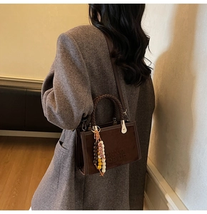 Détail d'un sac bandoulière en daim marron avec poignée tressée et pompon ethnique