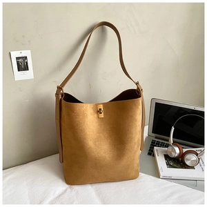 Detail of tan suede bucket bag with gold metal twist lock and wide leather strap