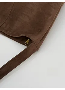Close-up of reinforced shoulder strap stitching and gold zipper on brown suede tote bag