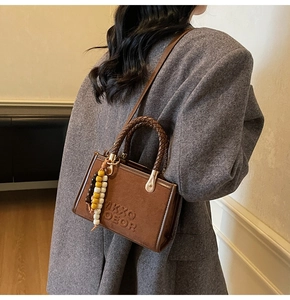 Détail du sac à bandoulière en daim marron avec poignée tressée et pendentif perlé