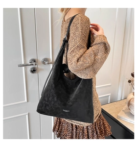 Close-up of black matte suede tote bag with shoulder strap worn by a female model