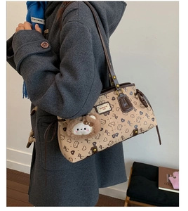 Detailed view of beige tote with brown trim and bear charm on female model