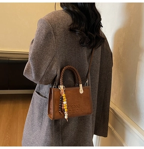 Détail du sac bandoulière en daim marron foncé avec poignée tressée et breloque en perles