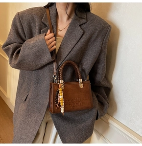 Détail du petit sac bandoulière en daim marron avec poignée tressée et pendentif perlé