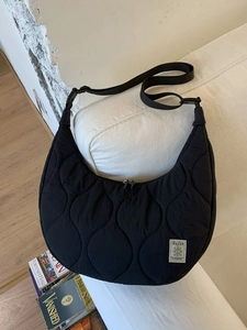 Borsa a tracolla trapuntata nera a mezzaluna su divano bianco per stile quotidiano