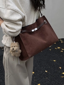 Brown suede tote bag with leather strap and metal lock shown in an autumn street style