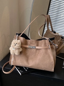 Brown suede tote bag with silver buckle and plush puppy charm in a minimalist setting