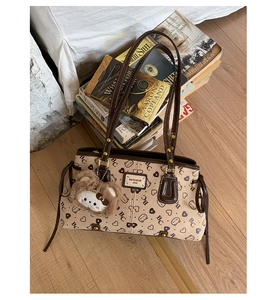 Close-up of beige tote bag with bear patterns, leather handles and plush bear charm