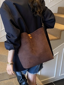 Brown suede bucket bag with gold twist lock shown in a casual lifestyle streetwear setting