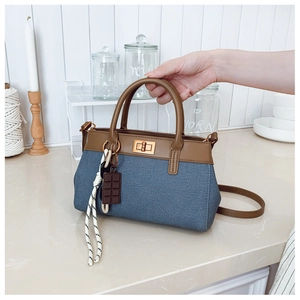 Detail view of blue denim bucket bag with brown leather handle and gold twist lock
