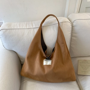 Brown suede tote bag with white SEEYOU woven label placed on a cream fabric sofa