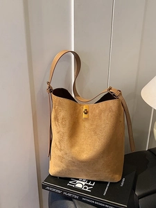 Minimalist camel suede bucket bag with gold rotary buckle on vintage art books