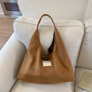 Detailed shot of a brown suede hobo bag with a white label on a cozy beige sofa