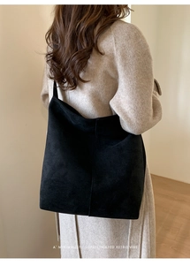Detail of minimalist matte black faux suede tote bag worn on shoulder in room setting