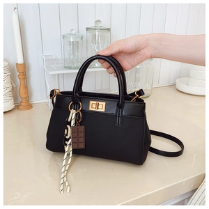 Detail of black leather bucket bag with gold clasp and chocolate pendant accessory