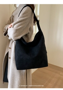 Detail of a black large capacity suede tote bag styled with a minimalist wool coat