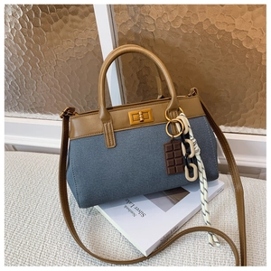 Détail du sac seau en denim bleu avec poignée en cuir marron et pendentif chocolat