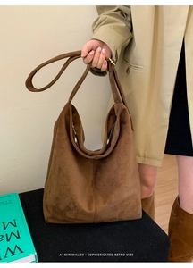 Detail of minimalist brown suede hobo tote bag held by a model in a camel coat