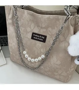 Detail of beige floral tote bag with pearl chain, metal strap and white pompom accessory