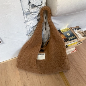 Detail of caramel brown teddy shearling tote bag with SEEYOU logo in cozy home setting