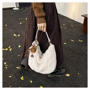 Vue détaillée du sac hobo en peluche blanc cassé avec pompon léopard sur feuilles d'automne