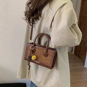 Details der dunkelbraunen Vintage-Umhängetasche mit Schriftzug und süßem Anhänger