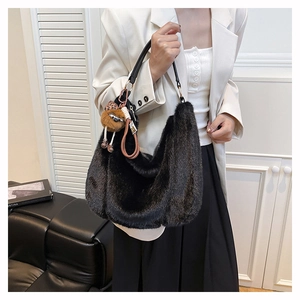 Détail du sac hobo en fausse fourrure noire avec poignée en cuir et breloque en peluche marron