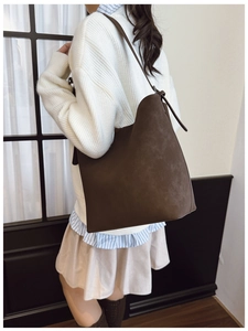 Deep brown matte suede bucket bag shown from a side view on a model in a minimal setting