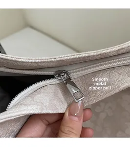 Detail of smooth silver zipper and textured beige fabric on a women's shoulder bag