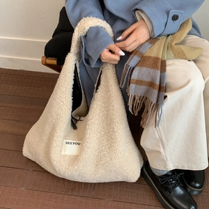 Detail of off-white faux shearling tote bag with 'SEEYOU' label on a blue coat background
