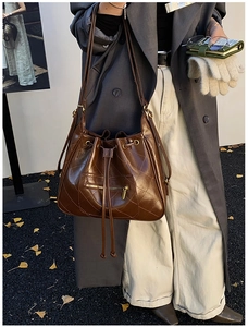 Detail of a dark brown quilted bucket bag with drawstring closure and metal zipper pocket