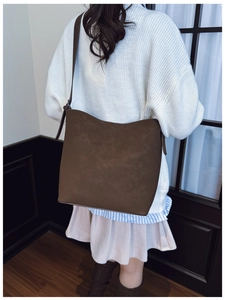 Detail of dark brown matte leather tote bag worn with casual oversized knitwear