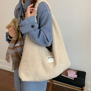 Detailed close-up of white faux shearling tote bag with SEEYOU label on blue coat