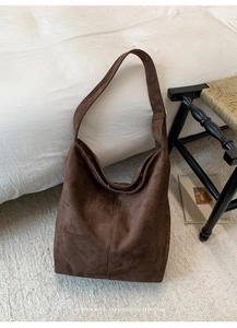 Close-up of dark brown suede bucket bag featuring wide shoulder strap and gold buckle