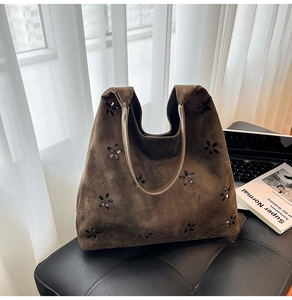 Detail of laser-cut floral pattern on dark brown suede tote bag in natural light