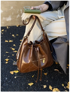 Detail of a brown quilted bucket bag with golden zipper and drawstring in outdoor setting