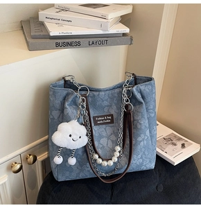 Detail of floral denim tote with pearl chain strap and cloud plush charm on sofa