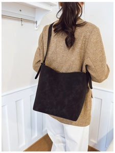 Detail of a large black suede bucket bag worn by a model in a smart casual business setting